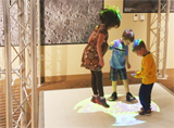Three children examine a photo of the moon projected onto the floor